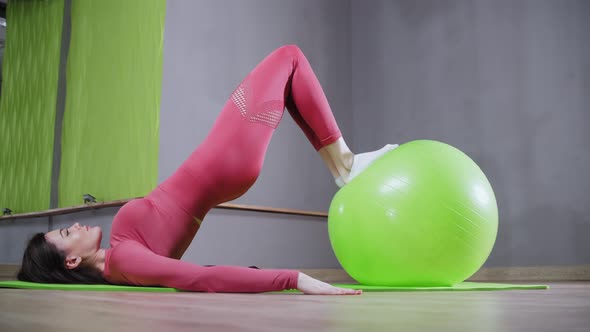 Young Woman in Sportive Costume Leaning Her Legs on the Fitness Ball and Doing an Exercise