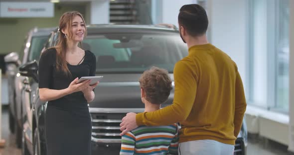 Back View of Adult Caucasian Man Choosing Automobile with Son in Car Dealership