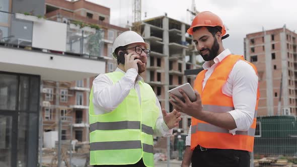 Happy Engineer Speaks on Mobile Phone on Construction Site and Checks the Work of the Worker