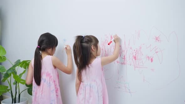 Asian young sibling kid girl enjoy paint on white wall in living room at home