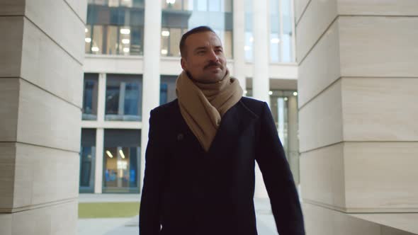 Smiling Businessman Wearing Scarf and Coat Walking Outside Office Building