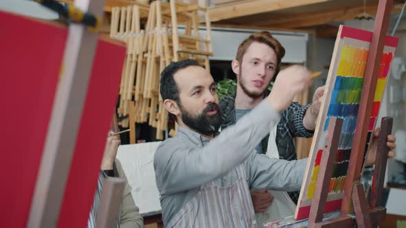 Skilled Artist Bearded Man Talking To Group of Art Students Teaching Drawing Picture in Studio