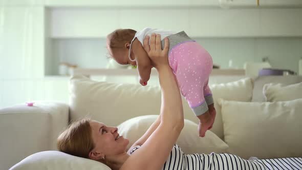 Mom Lying on Couch and Having Fun with Little Baby in Arms at Apartment Room Spbd