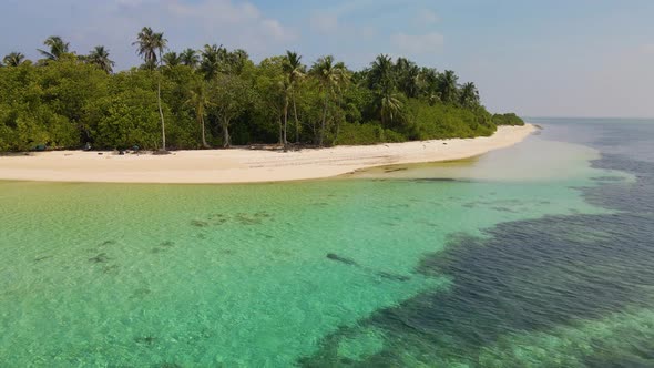 Drone flight over the Maldivian coast with many green trees, view from the ocean against the backdro