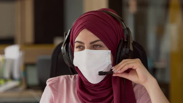 Beautiful modern muslim business woman in mask uses a microphone and headphones