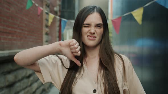 Portrait of Young Lady Showing Thumbsdown Hand Gesture and Looking at Camera with Unhappy Face