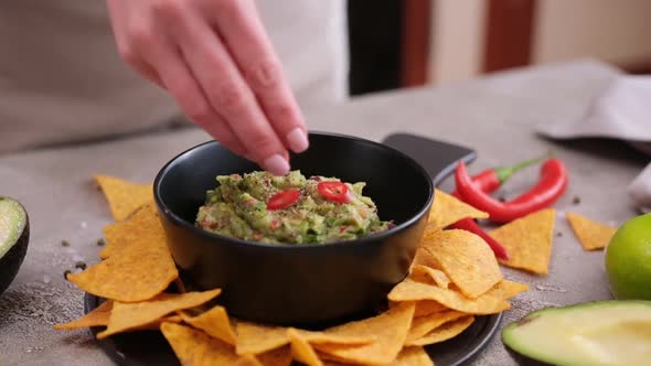 Woman Adding Pepper and Spices to Freshly Made Guacamole Dip Sauce in Marble Bowl Mortar