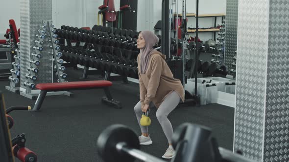 Muslim Woman Doing Weighted Squats with Kettlebell at Gym