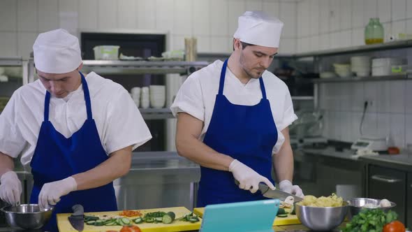 Front View Two Male Cooks Preparing Salad in Kitchen Talking