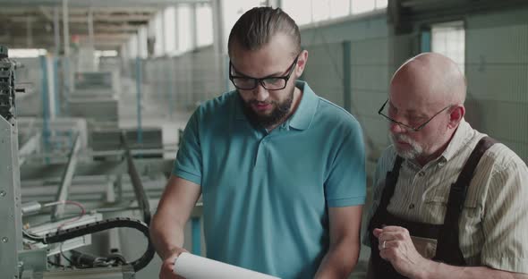 Two Engineers Stand at Factory Facility Have Discussion and Use Materials Notes