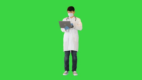 Young Asian Doctor is Working on Laptop Searching and Typing on a Green Screen Chroma Key