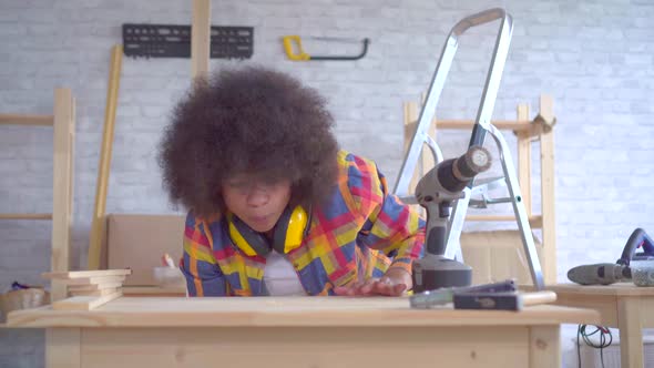 African Woman with an Afro Hairstyle Carpenter's Works on Wood in the Workshop