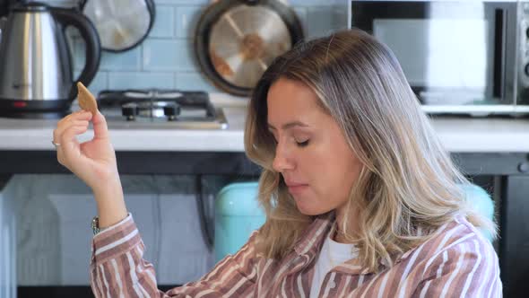 Cute girl in a plaid shirt and with long hair eating cookies and leafing through a book