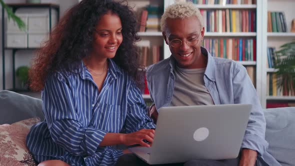 Biracial Couple Relax on Couch in Living Room Watching Video on Laptop Together