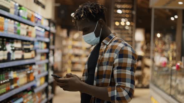 Handsome Man with Smartphone Walks at the Store Checking Shopping List