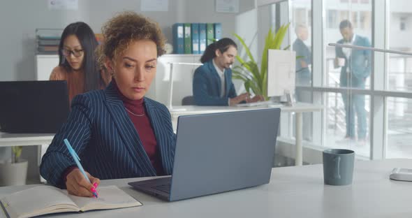 Confident Multiethnic Businesswoman with Curly Hair Using Laptop in Office