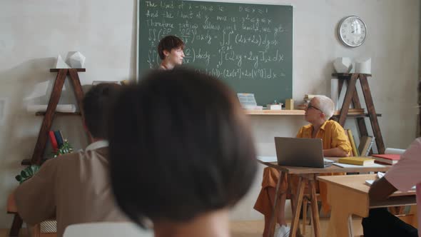 Cheerful Female Student Standing by Chalkboard and Talking on Lesson