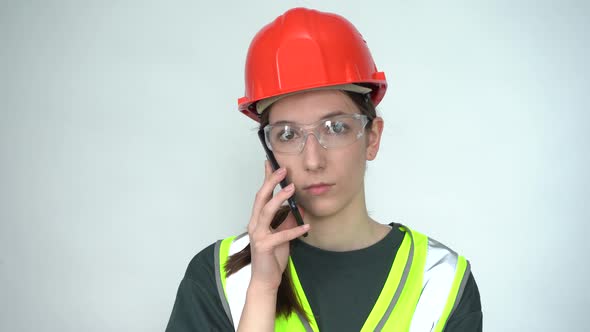 A Beautiful Young Female Construction Worker in a Safety Helmet is on the Phone