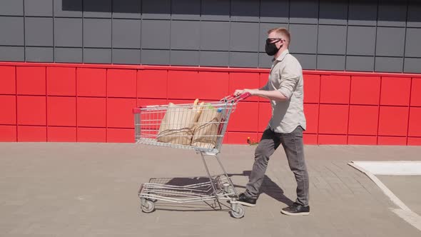 Man in Face Mask Pushing Cart of Groceries Outdoors