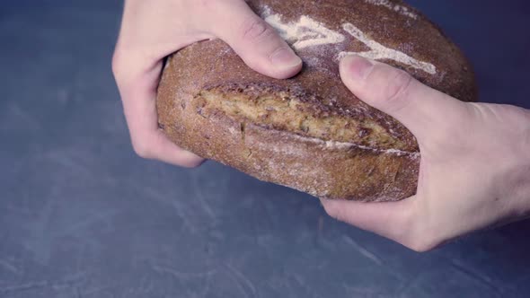 Men's hands break a loaf of round warm bread in half