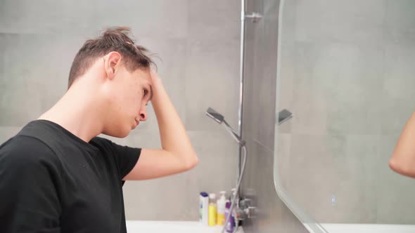 Hearingimpaired Young Man in Hearing Aids in the Bathroom Looks at Himself in the Mirror