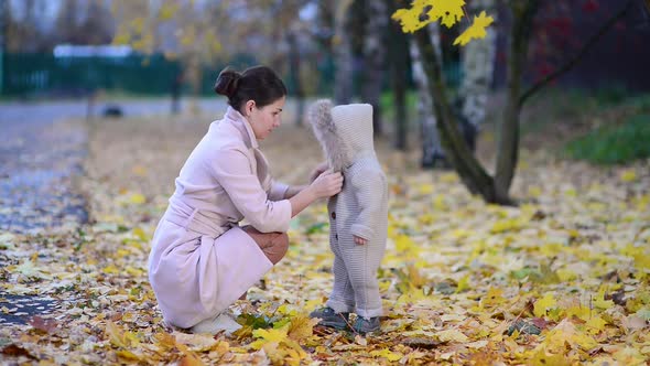 mother carefully fastens clothes to her baby daughter on the street in the autumn evening