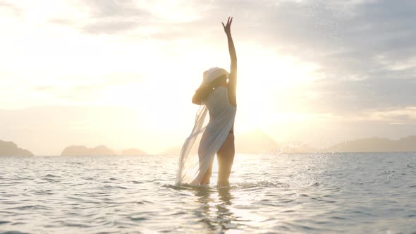 Woman In Thong Splashing Water In Sea Towards Glowing Sunset