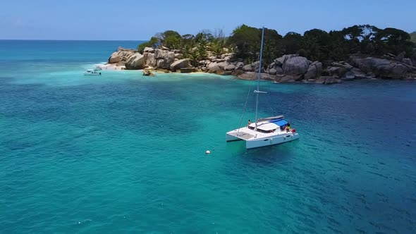 Paning aerial drone shot of a catamaran anchoring in the crystal blue water of the Seychelles in frr