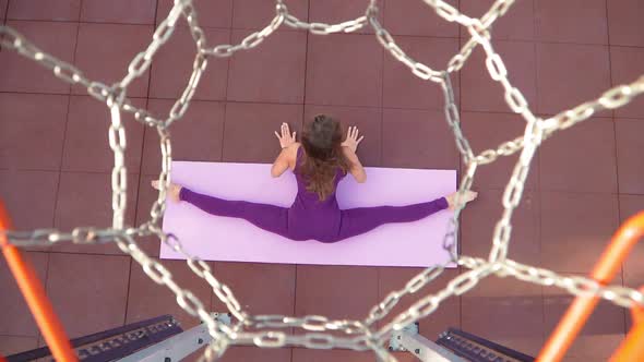 Young Athletic Woman in Sports Purple Tracksuit Does Exercise for Stretching While Sitting in Split