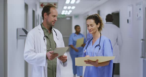 Caucasian male and female doctor talking in hospital corridor looking at tablet and patient files