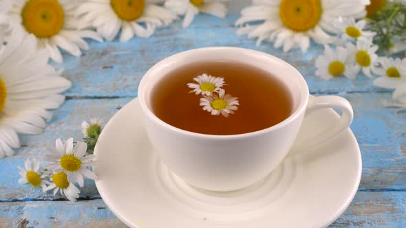 Composition with chamomile flowers and white cup of herbal tea on vintage light blue wooden table