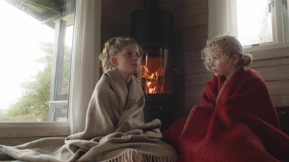 Young Children In Blankets By Fire At Home