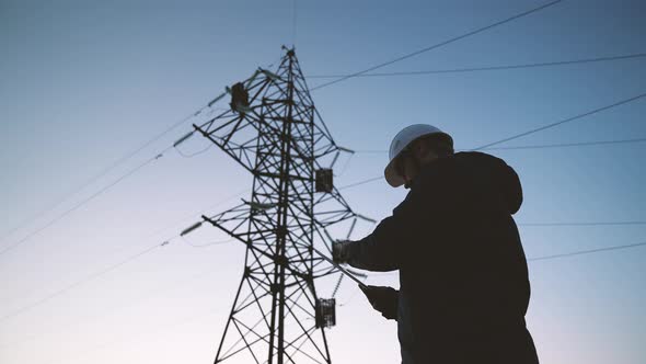 A Construction Engineer Power Engineer in a Protective Helmet Checks the Poles of Power Lines