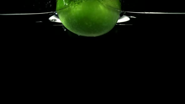 Slo-motion green apple falling into water