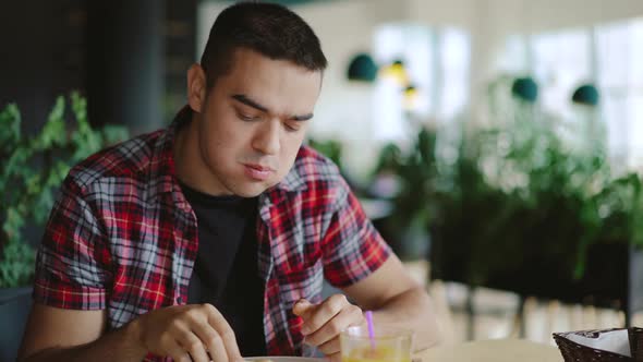 Young Man is Eating Pizza and Drinking Juice in the Cafe at Lunch