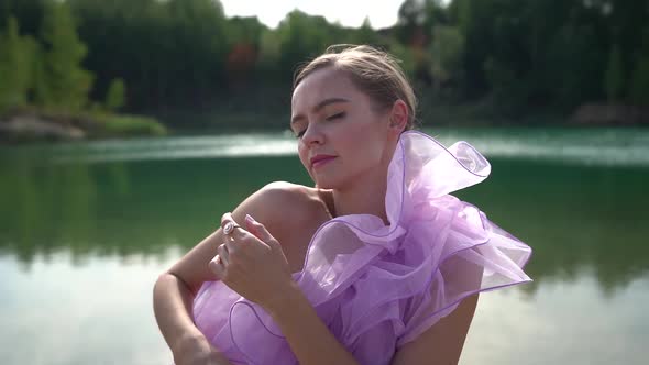 Cute Blonde in a Beautiful Lilac Dress Enjoys Nature, Posing on the Lake. Attractive Woman.