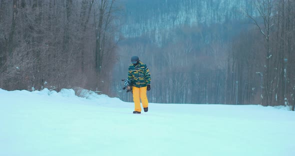 Man Climbs Up the Mountain with a Snowboard