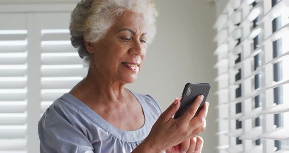 African american senior woman using smartphone and looking out of the window at home