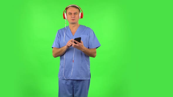 Medical Man in Big Red Headphones Turns on Music at Mobile Phone. Green Screen