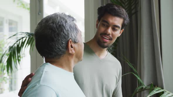 Biracial man smiling and keeping hand on shoulders of thoughtful father looking away at home