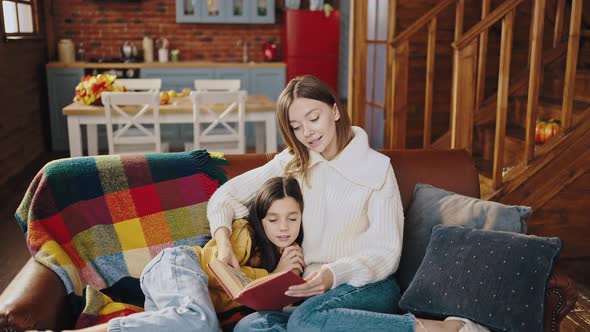 Young Mother Holding Book and Reading Fairy Tail to a Falling Asleep Preteen Daughter While Sitting