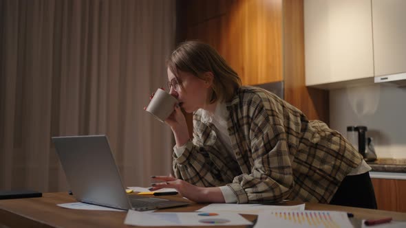 Beautiful Young Woman Working on Laptop Computer While Sitting at the Living Room Drinking Coffee