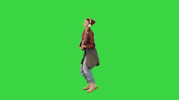 Young Girl in Stylish Clothes Starts to Dance While Listening to Music with Headphones on a Green