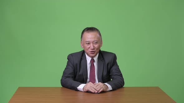 Mature Japanese Businessman Talking Against Green Background