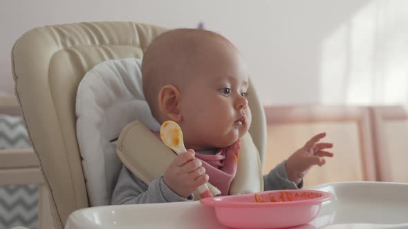 A newborn baby with a spoon tries to eat on its own. Feeding a newborn with pumpkin puree