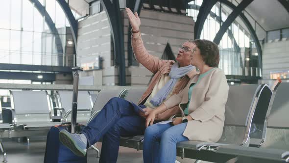 Portrait of Cheerful Elderly Couple Sitting in Waiting Area and Waiting for Their Flight Boarding