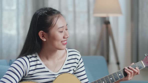 Close Up Of Smiling Asian Woman Composer Playing Guitar At Home