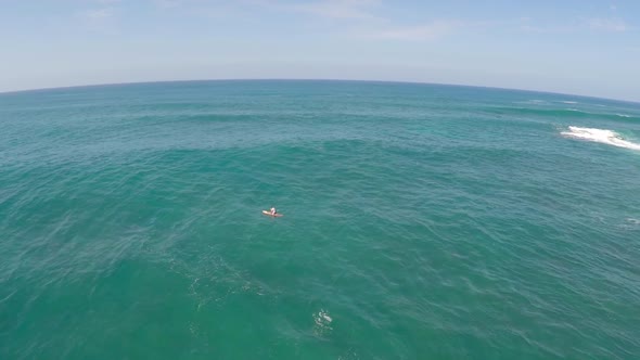Aerial view of man sitting on board waiting for waves stand-up paddleboard surfing in Hawaii