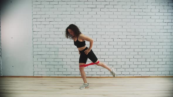 Workout in Sports Studio  Young Woman with Curly Hair Training with an Elastic Band on Her Legs