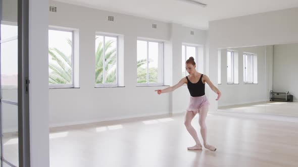 Caucasian female ballet dancer practicing ballet during a dance class in a bright studio